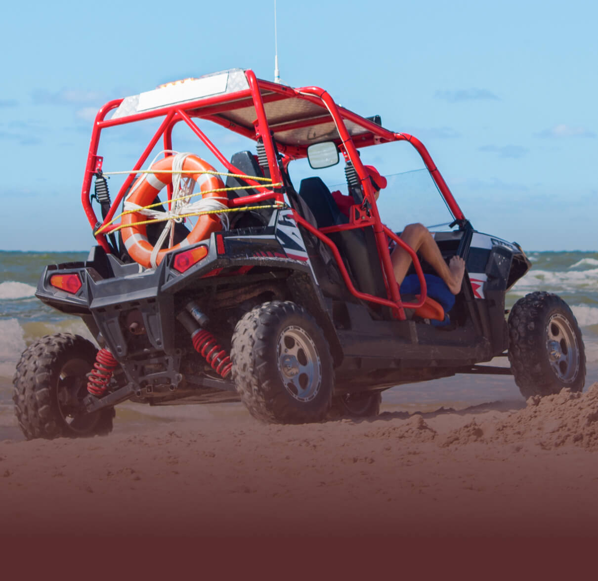 A dune buggy driving on a sandy beach. 